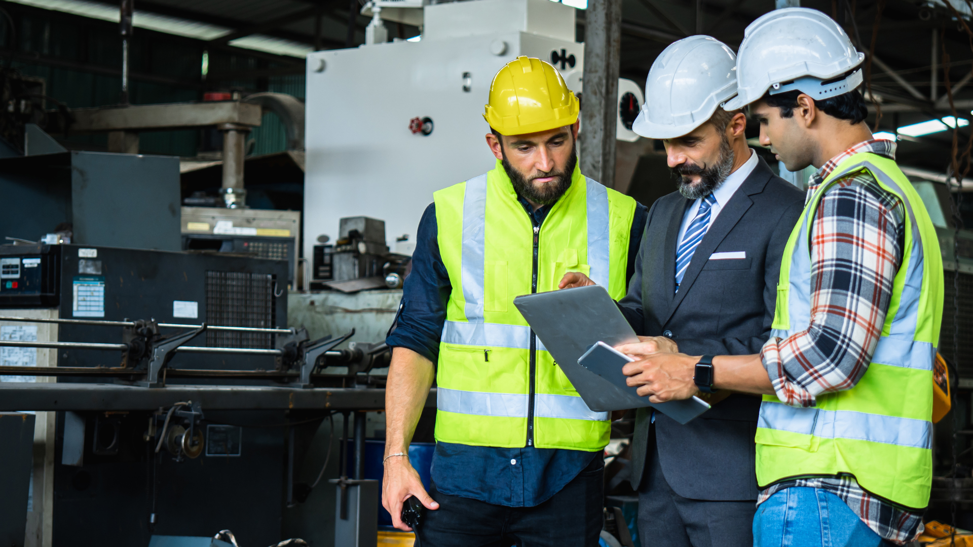 Consulente Net Srl e operai discutono misure di sicurezza sul lavoro in un impianto industriale a Torino, indossando caschi e giubbotti ad alta visibilità.