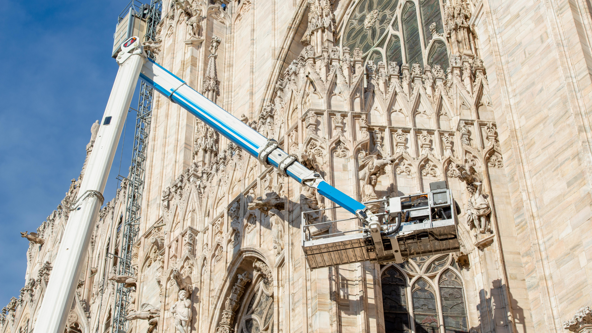 Operai a lavoro su una Piattforma di Lavoro Elevabile (PLE), durante lavori di restauro della facciata di una cattedrale gotica.
